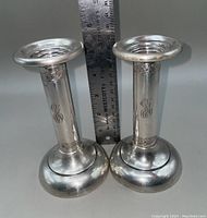 Pair of sterling silver candlesticks with weighted bases, monogram, and etched floral decoration, positioned beside a ruler for size reference.