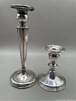 Photo showing both unmatched sterling silver candlesticks side by side, visible dents and reflective surface