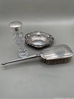 Three dresser items including sterling bon bon dish, sterling handled hair brush, crystal perfume bottle with sterling stopper.