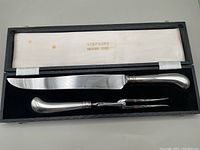 Carving knife and fork set neatly displayed inside a box with 'Simpsons Treasure House' branding on the fabric lining.