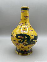Full view of the front side of the bright yellow ceramic Baijiu bottle showing the green dragon and red cloud motifs on the bulbous body and base band.