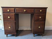 Front view of the 1950's era solid wood brown desk showing the seven drawers and brass knobs.