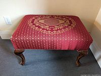 Full view of rectangular foot stool with red silk fabric upholstery, displaying gold diamond and floral medallion patterns on top, supported by wooden curved legs.