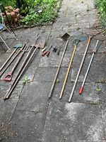 All garden tools laid out on stone pavement, showing total lot contents including rakes, spades, trowel, shears and pitchfork.