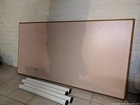Rectangular wooden kitchen table top resting against wall with four white detachable metal legs placed on floor next to it.