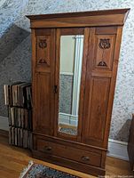 Front view of oak wardrobe showing center mirrored door, carved panel details on side doors, and bottom drawer