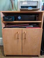 Front view of the wooden office storage unit with two doors and open shelves, showing storage contents including printer box and office folders.