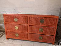 Six-drawer rattan cabinet painted reddish-orange with round metal handles, side angle view.