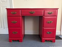 Front view of the solid wood red desk showing seven drawers with brass handles.