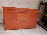 Front view of red metal two drawer filing cabinet against a cream wall and tiled floor.