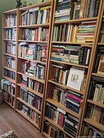 Two solid wood bookshelves filled with books and some framed pictures and sculptures in a room, showing the full height and width