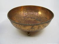 Copper bowl showing hammered texture and round shape with ball feet, placed on white background.