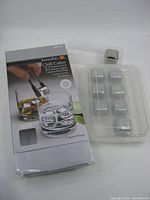 Box and 8 stainless steel chill cubes arranged on a clear tray with one cube outside the tray, showing their metallic finish and size.