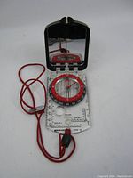 Full view of the vintage Brunton Type 15 compass open, showing mirrored lid, clear base plate, red bezel compass dial, and red string lanyard.