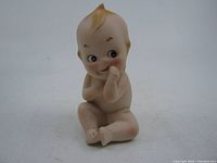 Front view of the ceramic Kewpie doll showing doll sitting with thumb near mouth and detailed facial features.