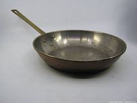 Copper frying pan, side perspective showing handle and depth of pan, with visible wear and patina on interior and exterior surfaces.