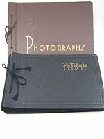 Photo of both photograph albums stacked, showing the brown and black covers with gold lettering and string ties.