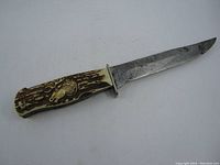 Full view of the folding knife with blade extended showing plastic antler-style handle with horse head emblem, blade shows wear.