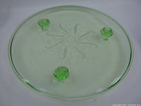 Top view of the green uranium glass cake plate showing the flat surface and the decorative feet visible through the glass.