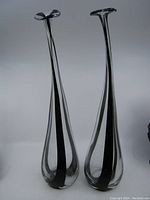 Full view of two slender hand blown glass vases, showing shape and black swirl pattern