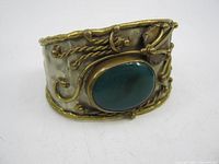 Front angled view of the handmade metal cuff bracelet showing the green oval stone and decorative metalwork.