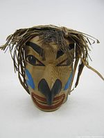 Front view of the wood carved hawk mask showing painted face, cedar strip hair and feather adornment.