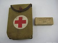 Canvas military first aid pouch front closed, showing red cross emblem and button closure with signs of wear and rust on button