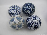 Photo showing four blue and white porcelain decorative balls with distinct patterns arranged on a white surface.