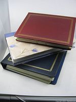 Three postcard albums stacked (red, beige, dark blue)