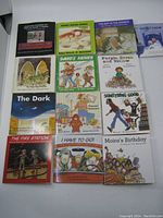 Top-down view of 13 small square children's books by Robert N. Munsch arranged in 3 rows on white surface showing front covers and titles.