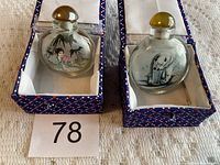 Two Chinese inside hand painted glass bottles in fabric-lined boxes shown from front side with painted scenes visible.