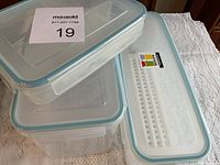 Stacked view of three clear rectangular plastic containers with lids featuring light blue seals and venting sections
