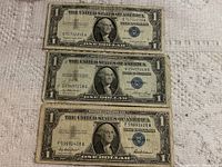 Three different one-dollar U.S. silver certificates laid out in a vertical arrangement on a textured surface, showing front sides with portrait of George Washington and blue seals.