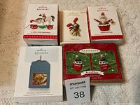Photo of five Hallmark Keepsake tree ornaments in their original boxes arranged on a surface.