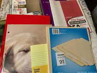 Overview of notebooks, folders, loose filler paper, and yellow lined notepad arranged on table for lot content display.