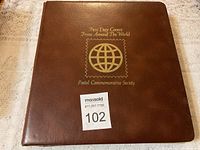 Closed brown album cover with gold embossed text and logo of Postal Commemorative Society's First Day Covers From Around The World.