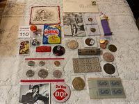 Overview of mixed lot items laid out on cloth surface showing coins, pins, stamps, and memorabilia