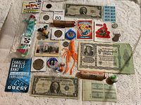 Various coins, currency bills, collectible cards, toys, tokens, stamps and small novelties displayed on textured fabric background.