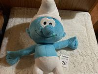 Front view of the stuffed Smurf plush toy lying on a surface, showing full body from hat to feet.