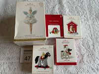 Photo showing five Hallmark Keepsake Christmas tree ornaments in original packaging on a white textured cloth.