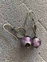 Close up of one earring showing silver hook, textured ring, and purple bead with a small black bead above it.