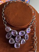 Full view of 16 inch necklace with nine faceted light purple amethyst quartz stones set in silver chainlink setting on brown display.