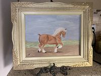 Front view of the framed painting showing a horse in a natural background with carved beige frame