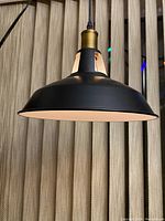 Photo showing the black metal shade with white inside, hanging lamp suspended by black cord with brass socket holder