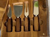 Four cheese cutting tools with carved wooden handles and stainless steel blades and prongs, neatly arranged in a wooden box with slots for each tool.