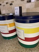 Photo showing two large striped tin containers side by side on a kitchen counter under tile backsplash.