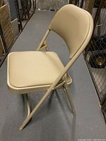Side view of beige Kleton padded folding chair showing cushioned seat and backrest with metal frame.