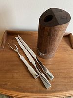 Wood base with three white-handled stainless steel carving utensils displayed on wooden tray