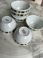 Set of six white small dessert bowls with geometric pattern in black, gold, and gray around the exterior.