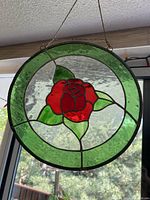 Front view of circular stained glass sun catcher hanging by chain, showing red rose center and green border.